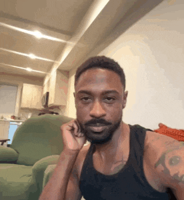 a man with a beard is sitting in a chair with his hand on his chin and looking at the camera .