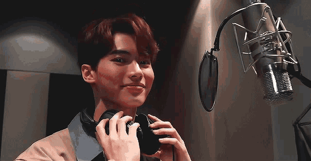a young man is wearing headphones in front of a microphone in a recording studio .