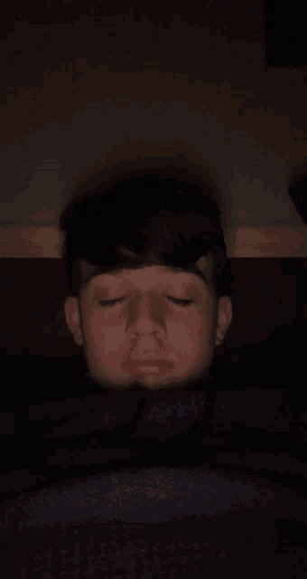 a young boy with his eyes closed is laying in a dark room