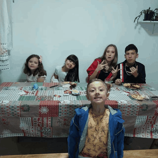 a group of children sit at a table with a christmas tablecloth