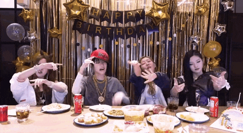 a group of people are sitting at a table with plates of food and a happy birthday banner