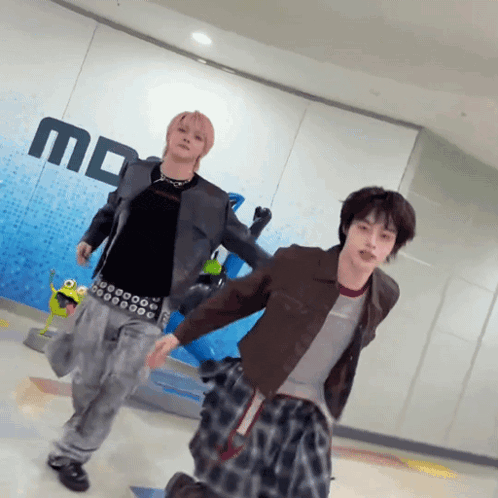 two young men are dancing in front of a wall that has the letter m on it