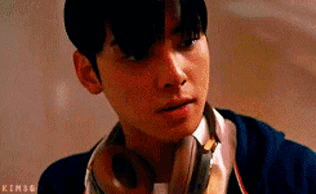a young man wearing headphones around his neck is looking at the camera .
