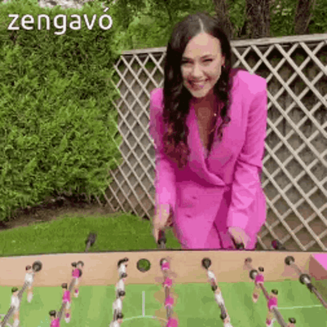 a woman in a pink suit is playing a foosball game outside .