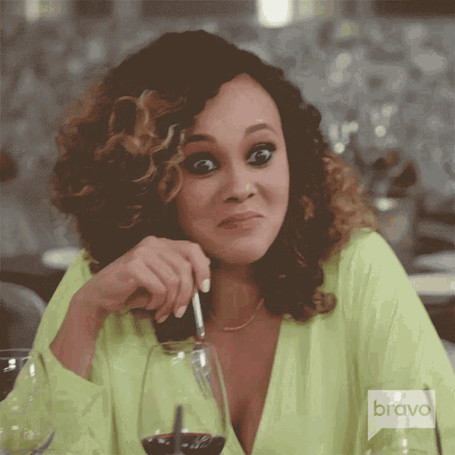 a woman is sitting at a table with a glass of wine and a bravo logo