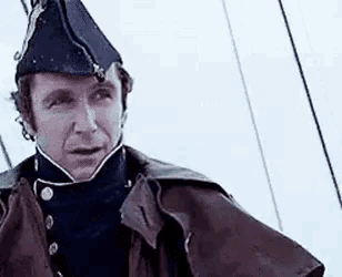a man in a military uniform is standing on a boat wearing a hat .