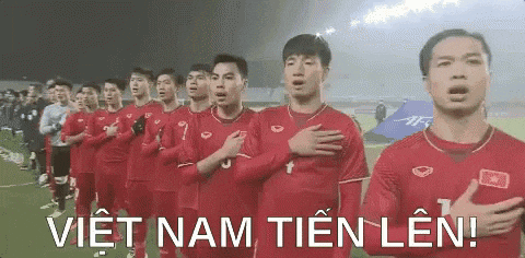 a group of soccer players are standing in a row on a field with their hands on their chests .