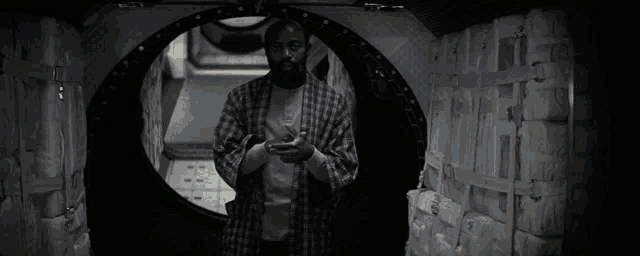 a man in a plaid shirt is standing in a dark tunnel