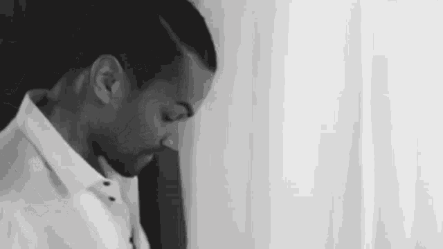 a man in a white shirt is standing in front of a window and looking down .