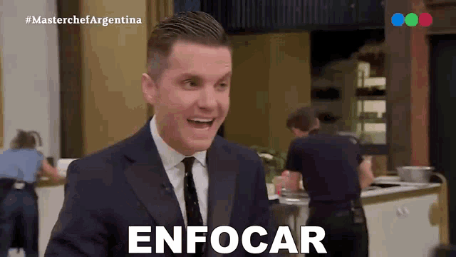 a man in a suit and tie says " enfocar " in front of a kitchen