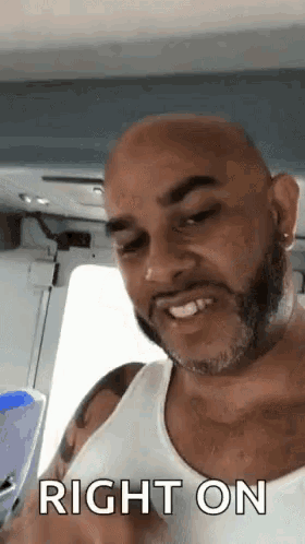 a man with a beard and a white tank top is smiling and says right on