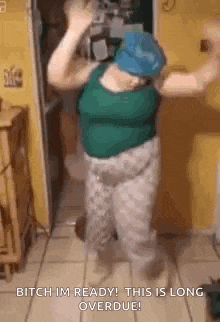 a woman in a green tank top and gray pants is dancing in a kitchen .