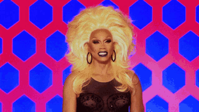 a drag queen with blonde hair and hoop earrings is smiling