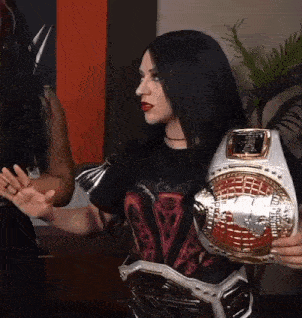 a woman in a black shirt is holding a wrestling championship belt .