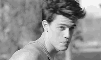 a black and white photo of a young man wearing a tank top and looking at the camera .