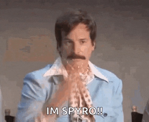 a man with a mustache is sitting at a table with his hands folded and says `` im spyro ! ''