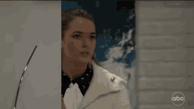a woman in a white jacket is standing in front of a painting .