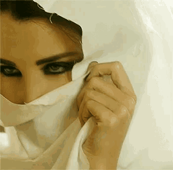 a woman is covering her face with a white cloth and her hands .