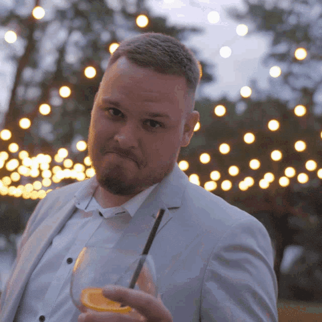 a man in a suit holds a drink with a straw in his hand