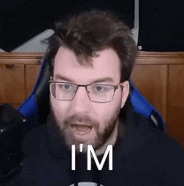 a man with glasses and a beard is sitting in a chair and saying `` i 'm '' .