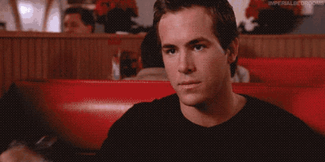 a man in a black shirt is sitting in a red chair in a diner .