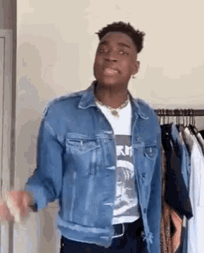 a young man in a denim jacket is standing in front of a clothes rack .