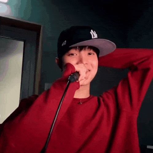 a man wearing a red shirt and a white hat is holding a microphone in front of his face