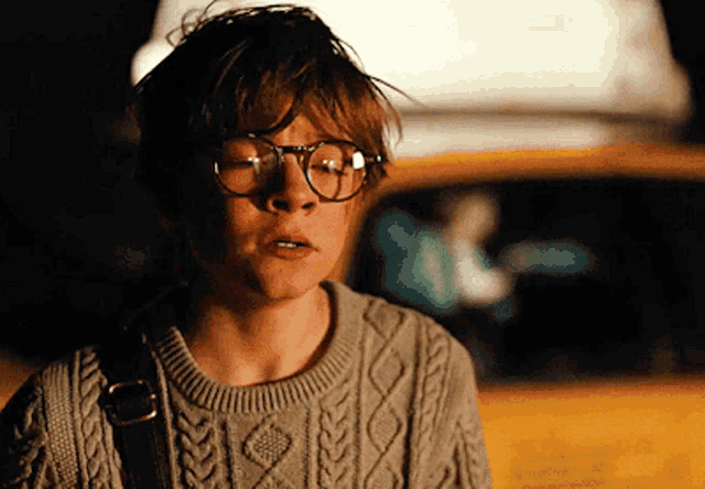 a young boy wearing glasses and a sweater is looking at the camera