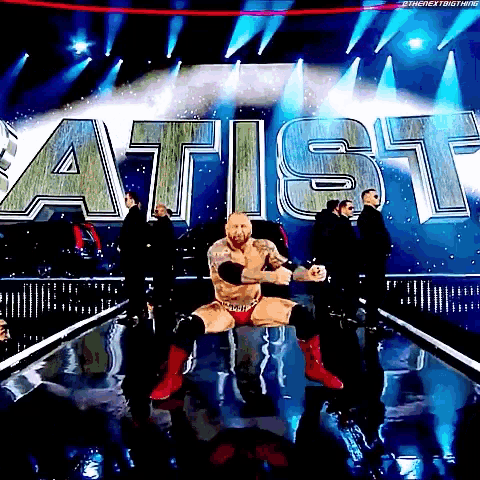 a wrestler is kneeling down on a stage in front of a sign that says artist