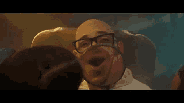 a bald man wearing glasses and a mask is sitting in a chair .