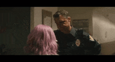 a man in a police uniform is talking to a woman with purple hair in a hallway .