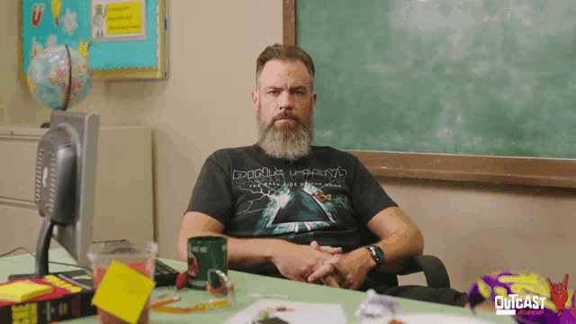 a man with a beard sits at a desk wearing a dark side of the moon t shirt