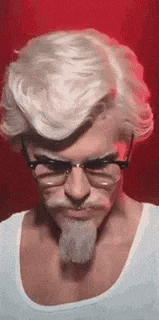 a man with white hair , glasses and a beard is dressed as a kfc chicken .