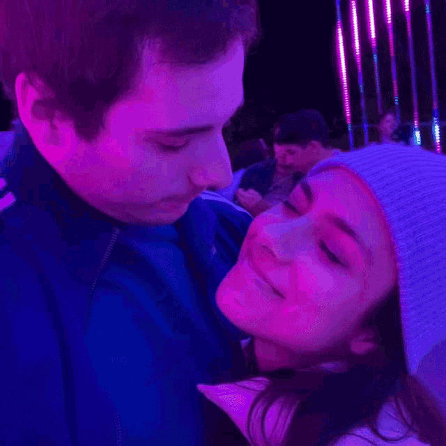 a man kissing a woman on the cheek in front of purple lights