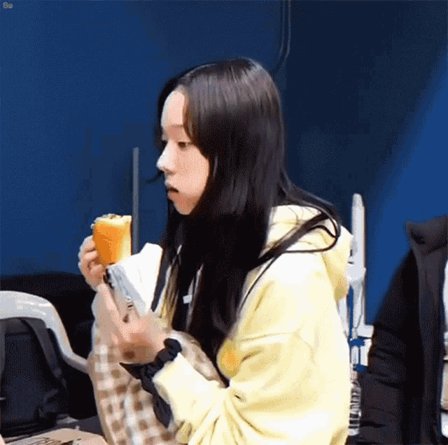a young girl in a yellow hoodie is eating a sandwich .
