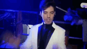 a man in a white suit is standing in front of a microphone on a stage .