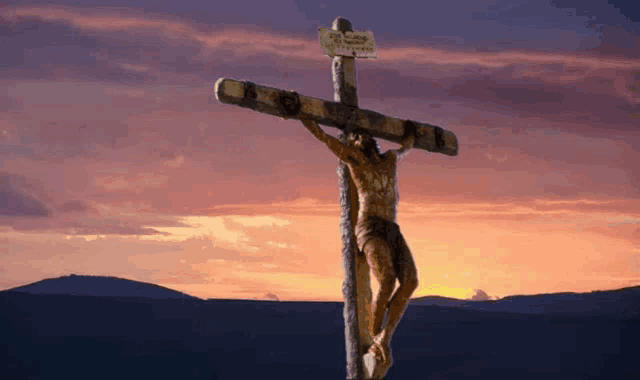 a statue of jesus is hanging on a cross with a sign that says " jesus is risen " on it