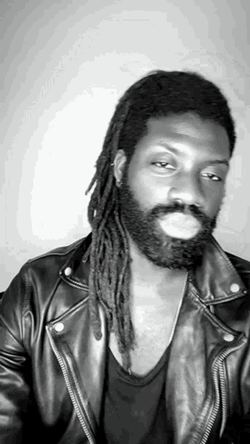 a black and white photo of a man with dreadlocks and a beard wearing a leather jacket
