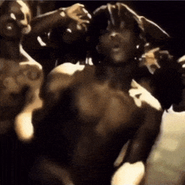 a group of men without shirts are dancing in a dark room