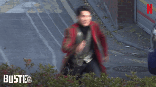 a man in a red coat and black vest is running down a street with the word busted on the bottom right