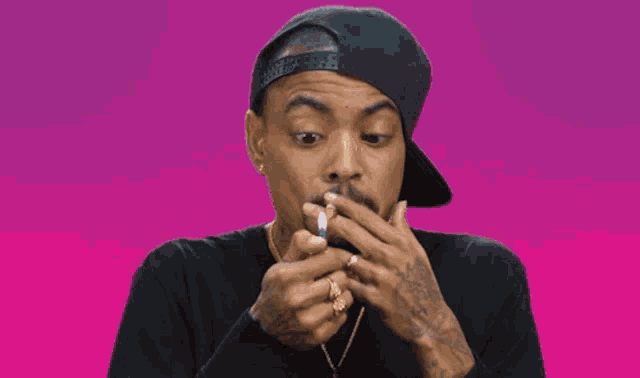 a man wearing a black shirt and a gold necklace smoking a cigarette