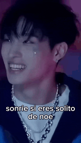 a young man wearing a necklace is smiling and crying with the words sonrie si eres solito de noe below him .
