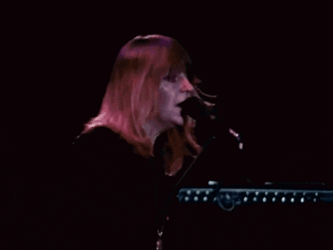 a woman is singing into a microphone on a stage while playing a keyboard .