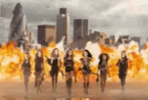 a group of women are walking in front of a city skyline with fire coming out of the sky .