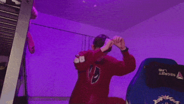 a man in a red hoodie is dancing in a room with purple lights
