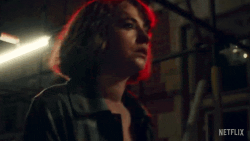 a woman in a leather jacket is standing in front of a red light .