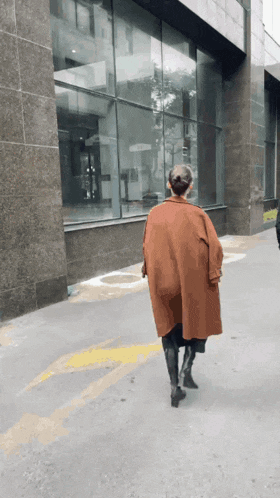 a woman in an orange coat is walking down a sidewalk