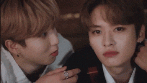 two young men are sitting next to each other and one of them is putting a ring on the other 's finger .