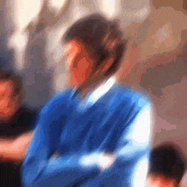 a blurry picture of a man in a blue sweater with his arms crossed