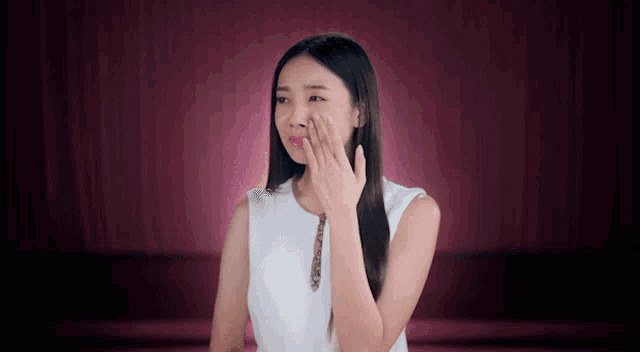 a woman covering her face with her hand while wearing a white shirt